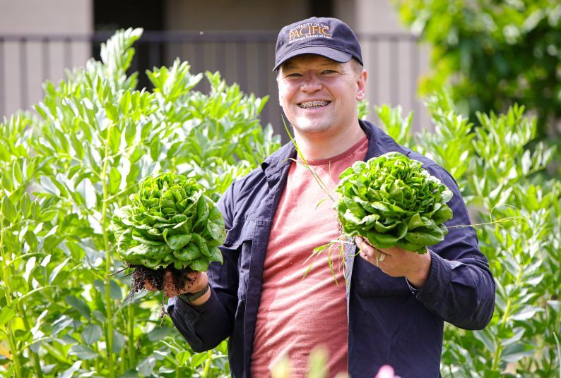 A man holds vegetables in a garden